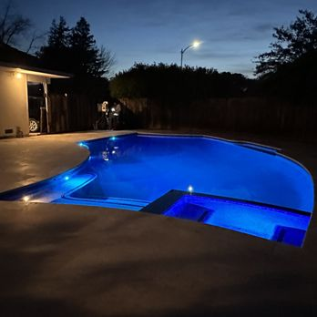 A beautifully lit pool at dusk with glowing blue water and a surrounding patio, serviced by Olivera Pool Services in San Jose.